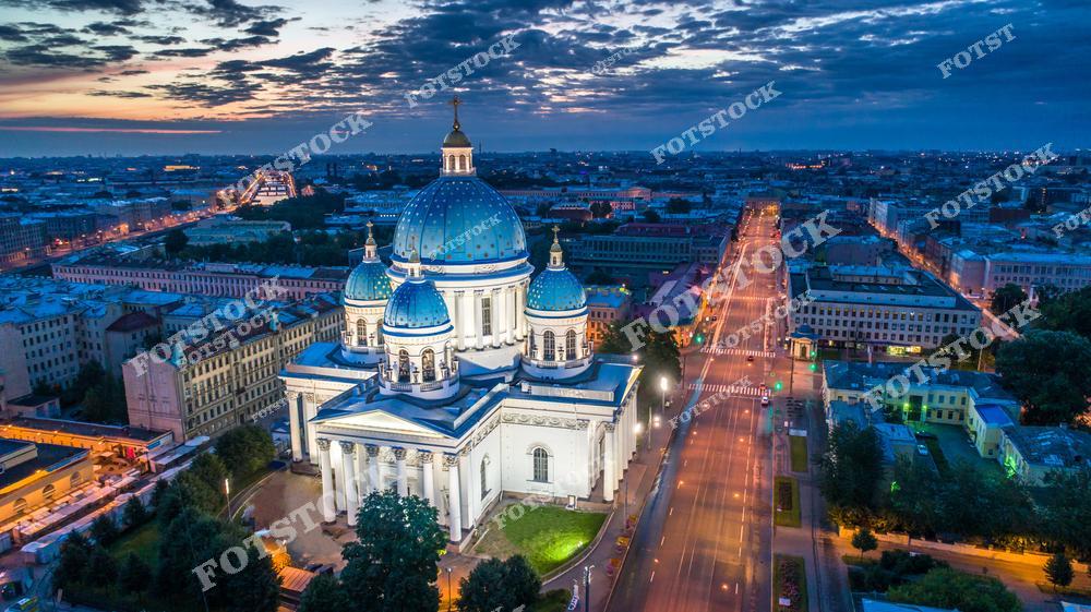 На фотографии изображён Троицкий собор, подсвеченный огнями ночного Санкт-Петербурга. Его голубые купола с золотыми звёздами выделяются на фоне городской панорамы. Прямые линии освещённых улиц подчёркивают симметрию и гармонию городского пространства. Ночная атмосфера делает пейзаж очень живописным.